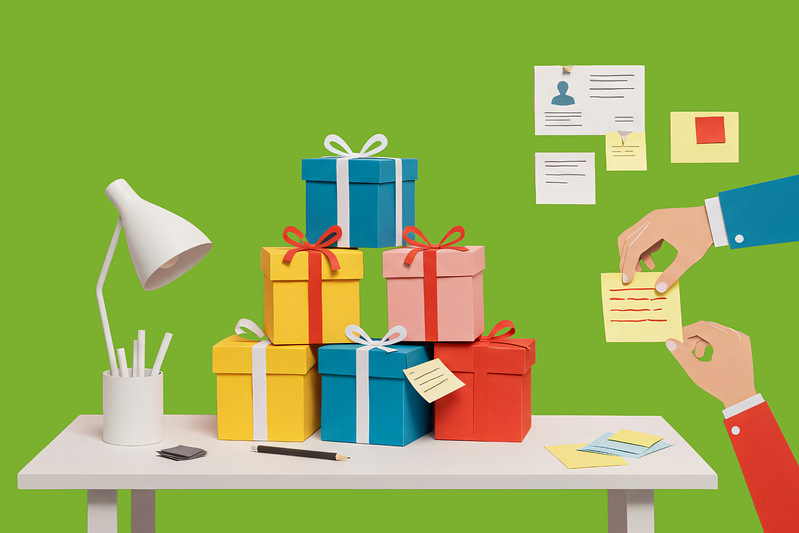 A desk with stacks of gifts and post it noes on the wall while two employees plan out purpose-driven corporate gifting