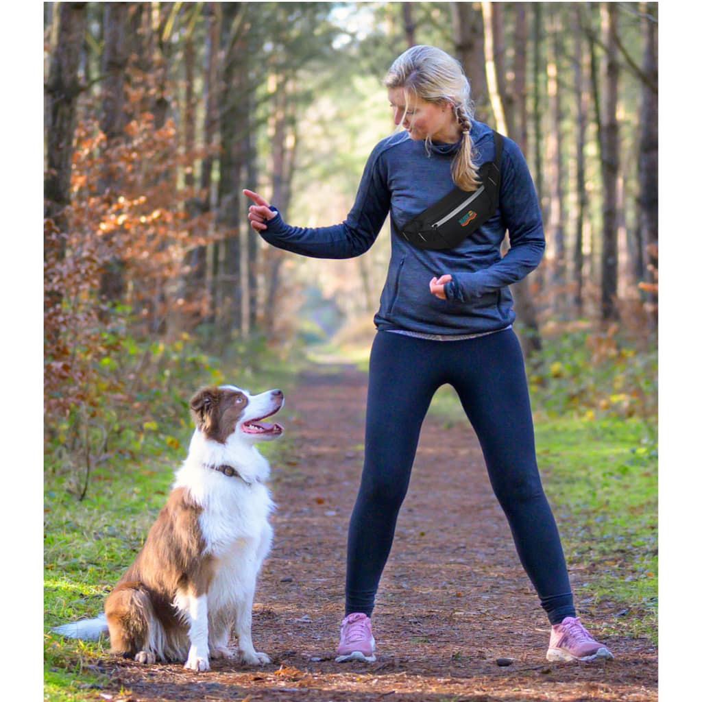 Sportive woman training her dog to sit, standing outdoors on a trail at park or forest, viewed from the front