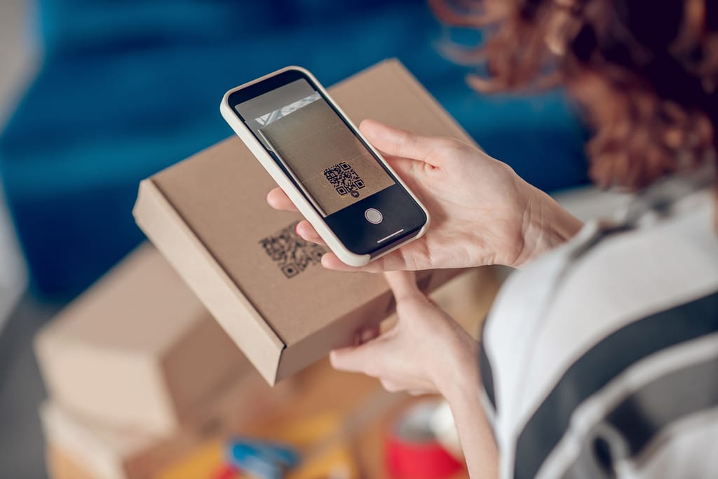 Cropped photo of a female worker aiming her camera at the QR code on the cardboard box